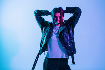 Stylish beautiful young woman model in fashionable outerwear with a black leather jacket and a white T-shirt in the studio on blue background with pink light. Creative color gradient and female style