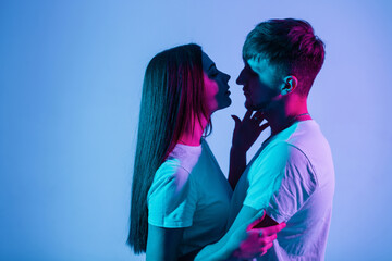 Beautiful couple of people in love with creative colorful blue and pink light. Pretty fashionable woman with handsome stylish man in white t-shirts kissing in studio
