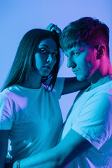 Fashionable pretty creative couple in white t-shirts in studio with neon pink lights. Stylish woman model with boyfriend indoors