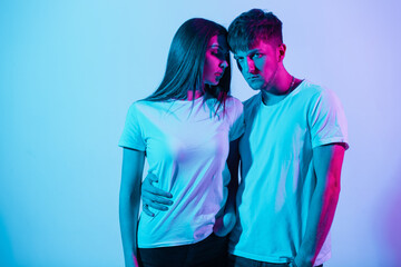 Stylish beautiful young couple in white t-shirts with neon and pink light in the studio. Pretty...