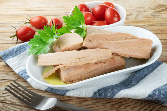 Tuna fillets in olive oil with parsley and cherry tomatoes on wooden background.