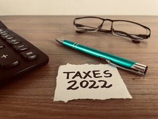 Taxes 2022 text with pen, calculator and glasses on office desk, business and finance concept