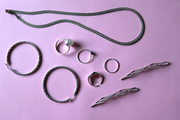 Arrangement of various silver jewelry accessories on pink background. Flat lay.