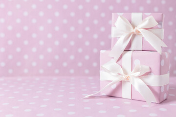 Gift boxes tied with satin ribbons stand on a pink background.