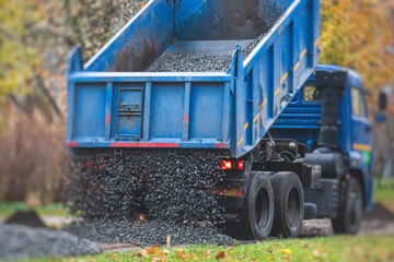 Dump truck, tractor and bulldozer unloading gravel, road metal, rubble and crushed stone cement material during landscaping improvement and new pedestrian walk road construction site - obrazy, fototapety, plakaty