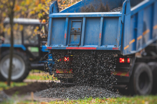 Dump truck, tractor and bulldozer unloading gravel, road metal, rubble and crushed stone cement material during landscaping improvement and new pedestrian walk road construction site