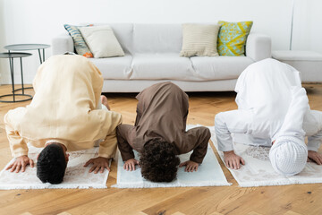 Arabian men and boy bending on rugs while praying at home.