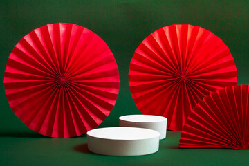White podium or pedestal with decorative red paper fans on a green background. Product presentation...