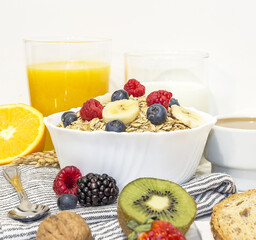 healthy breakfast of granola with blueberries, bananas and raspberries in a white porcelain bowl, with fruit, nuts, milk, coffee and wheat toast. front view
