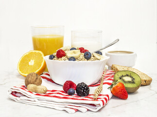 healthy breakfast of granola with blueberries, bananas and raspberries in a white porcelain bowl, with fruit, nuts, milk, coffee and wheat toast. front view