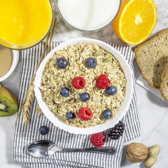 healthy breakfast of granola with blueberries and raspberries in a white porcelain bowl, with fruit, milk, coffee and wheat toast. aerial view