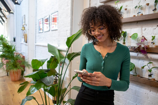 Smiling Woman Looking At Smart Phone In Flower Shop