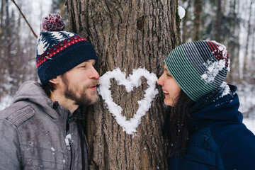 Young couple outdoor portrait. Beautiful pretty girl kissing handsome boy with beard in mittens in park in winter. Sensual photo