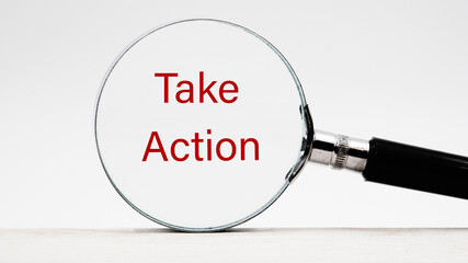 Business concept. Phrase TAKE ACTION through a magnifying glass on a light background