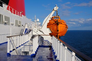A red lifeboat hangs on the ferry. The white deck of a large passenger ferry. 