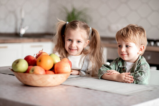 Healthy food at home. Happy two cute children: girl and boy eating healthy fruits: red green apples and oranges at the table in the kitchen. Healthy food baby dieting concept. selective focus