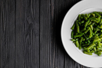 Serving of green beans white plate on dark wooden board, low key photo with copy space.