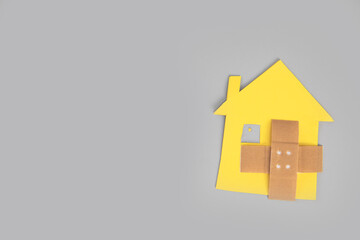 Closeup of broken house figure with crossed band aid on grey background top view, copy space, divorce, relationship problems, moving house, mortgage,