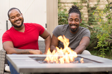 Smiling male couple sitting by fire pit © Cultura Creative