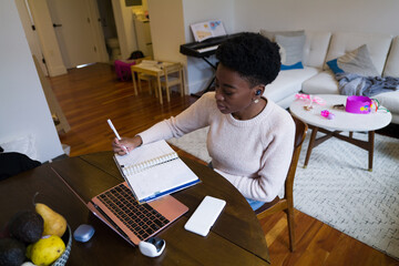 Woman using laptop and writing in notepad