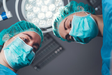 From below female surgeons in medical uniform using professional tools while standing under bright...