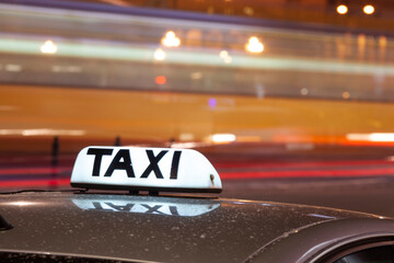 Shining Taxi inscription close up against passing cars on night street of big cit