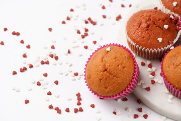 Several homemade white and pink muffins on marble board on white surface with heart-shaped red and white sugar decoration