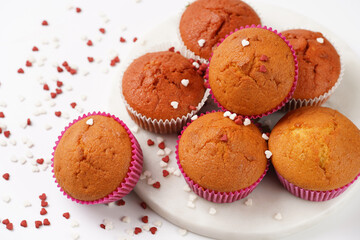 Several homemade white and pink muffins on marble board on white surface with heart-shaped red and white sugar decoration