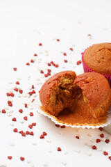 Several homemade white and pink muffins on marble board on white surface with heart-shaped red and white sugar decoration