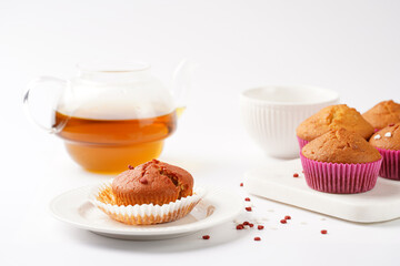 Several homemade white and pink muffins on marble board on white surface with heart-shaped red and white sugar decoration and tea-pot