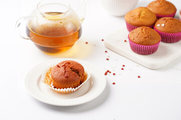 Several homemade white and pink muffins on marble board on white surface with heart-shaped red and white sugar decoration and tea-pot