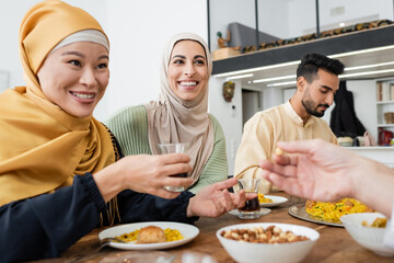 cheerful asian woman holding cup of tea during dinner with muslim family.