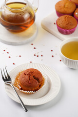 Several homemade white and pink muffins on marble board on white surface with heart-shaped red and white sugar decoration and tea-pot