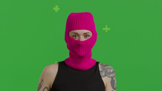 Close-up of young woman wearing pink knitted balaclava swipes finger at display of phone. Female model over green screen background, Chroma Key. 4k video footage