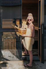 Frau mit Aufgussbottich vor der Sauna