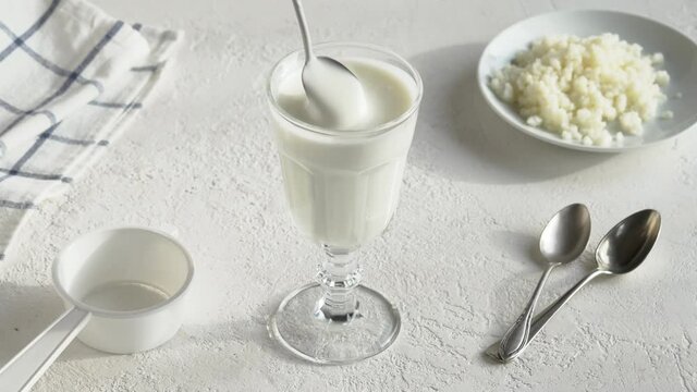 Mixing fresh homemade milk kefir with a spoon, with kefir grains in the background