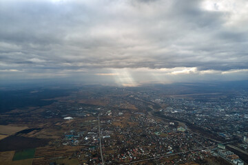 Aerial view from high altitude of distant city covered with puffy cumulus clouds flying by before rainstorm. Airplane point of view of landscape in cloudy weather