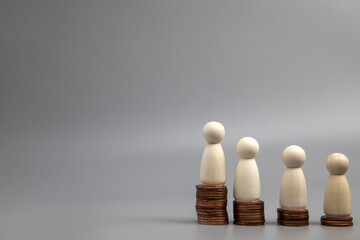 Miniature people standing on piles of different heights of coins. The concepts of person and...