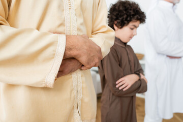 Young muslim man praying near blurred son at home.