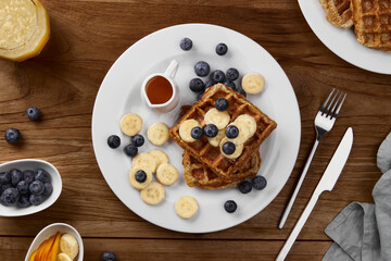 Oatmeal Belgian waffles topped with banana and blueberry on rustic wooden table. Healthy breakfast diet recipe