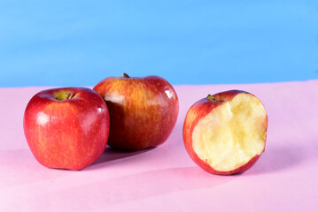 beautiful red apples seen from the side isolated on pink and blue background, bitten apple