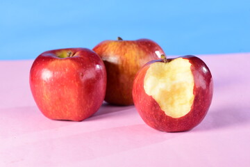 beautiful red apples seen from the side isolated on pink and blue background, bitten apple