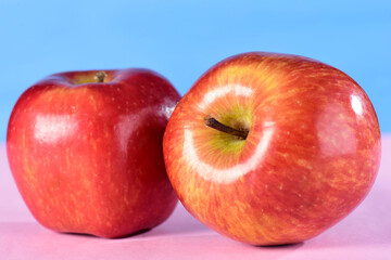 beautiful red apples seen from the side isolated on pink and blue background, bitten apple
