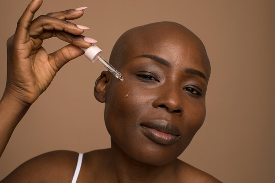 Studio Portrait Of Woman With Shaved Head Applying Oil On Face