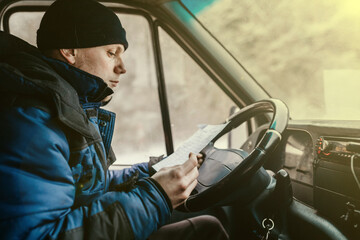 forwarder driver sits behind the wheel of a car and examines waybills documentation for the cargo. - obrazy, fototapety, plakaty