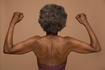 Rear view of shirtless senior woman flexing muscles