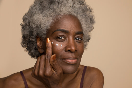 Studio Portrait Of Senior Woman Applying Eye Cream