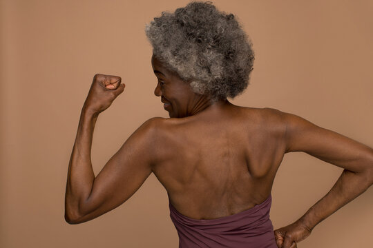 Rear view of shirtless senior woman flexing muscles