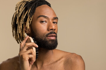 Studio portrait of young man with dreadlocks brushing beard