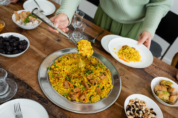 Cropped view of muslim woman serving pilaf near tasty food on table.